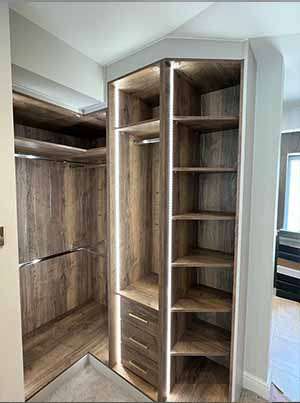 Custom-built L-shaped wardrobe with wooden compartments and drawers, part of a bespoke storage solution.